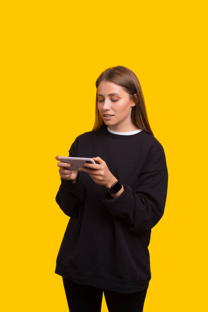 Photo of girl teenager playing online games on mobile phone over yellow background - Photo, Image