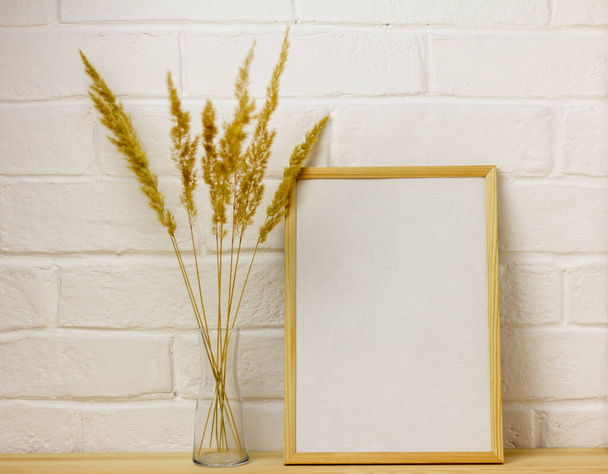 Malli tyhjästä valokuvakehyksestä ja syksyn kukkakimppu kuivatuista yrteistä läpinäkyvässä maljakossa puupöydällä, jossa on kopio tilasta - Valokuva, kuva