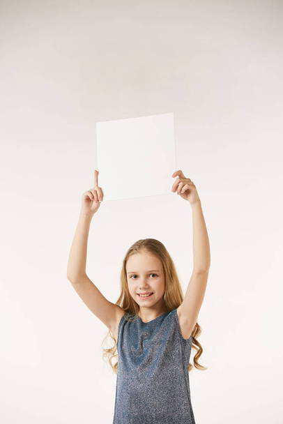 A girl in a gray dress stands on a white clean background with a white clean sign in her hands. Blank surface for advertising and lettering. - Foto, afbeelding