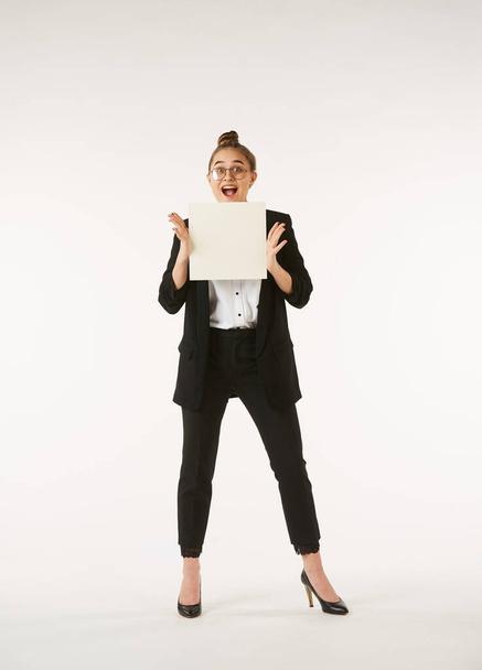 A young girl in office clothes is holding a white blank sheet of paper. Use for advertising and text. - Foto, imagen