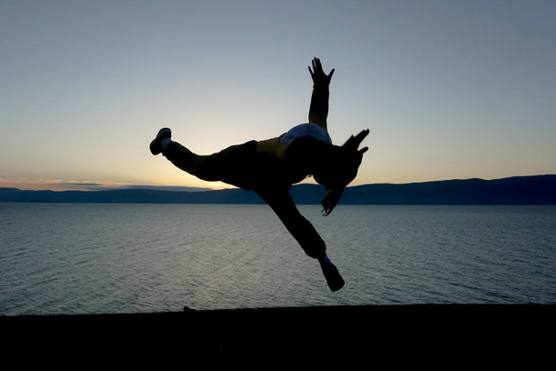 Silhouet van een man die acrobatische oefeningen doet in de natuur in Baikal - Foto, afbeelding