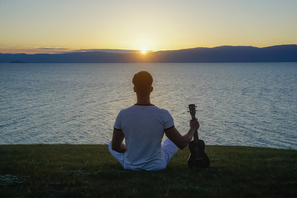 Guy in white clothes with ukulele at sunset - Foto, afbeelding