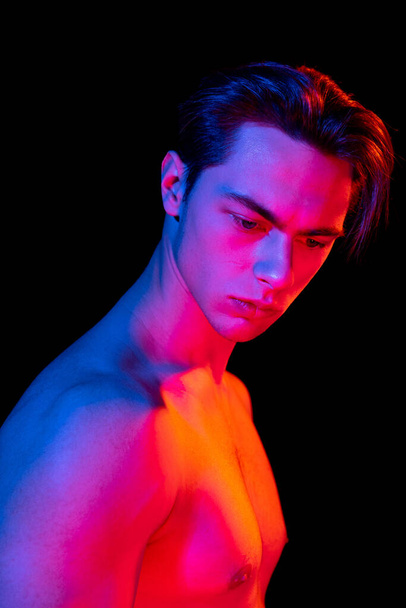 Handsome young mans portrait isolated on dark studio background in pink neon, Concept of human emotions, facial expression - Photo, Image