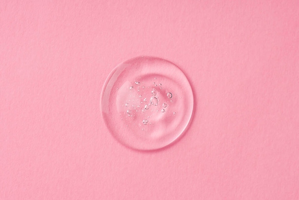 Transparante druppel cosmetische product serumgel. Vloeibare textuur met belletjes op roze achtergrond in bovenaanzicht. Huidverzorgingsproducten, natuurlijke cosmetica. Schoonheidsconcept voor gezichts- en lichaamsverzorging - Foto, afbeelding