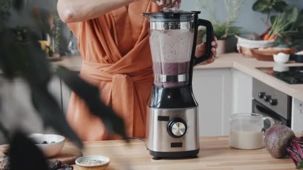 Mid-section tracking of unrecognizable young woman making healthy and delicious smoothie in cozy kitchen with fresh vegetables and fruit - Filmagem, Vídeo