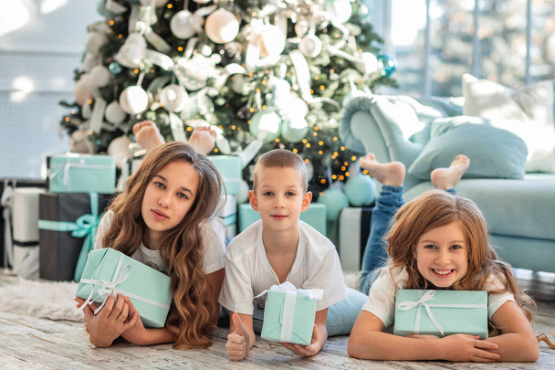 Children at Christmas tree and fireplace on Xmas morning. Family with kids celebrating Christmas at home. Boy and girls opening presents. Holiday gifts for kids. - Foto, imagen
