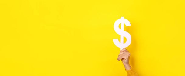 σύμβολο δολαρίου στο χέρι πάνω από κίτρινο φόντο, πανοραμική διάταξη - Φωτογραφία, εικόνα