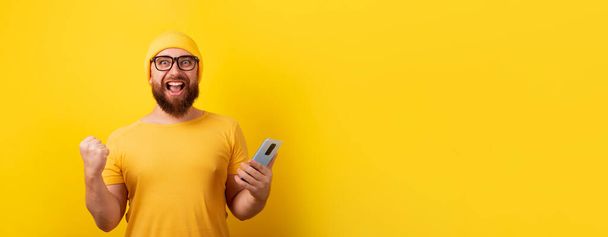 man holding phone over yellow background, winner concept, panoramic layout - Фото, изображение