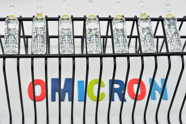 Slovo omicron, varianta covid 19, mezi mřížemi, obklopeno lahvičkami s vakcínou - Fotografie, Obrázek