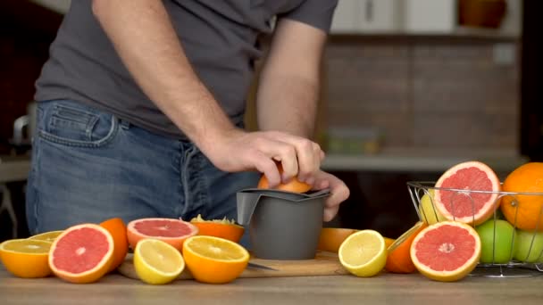 Un hombre exprime jugo de naranja con exprimidor de cítricos. Primer plano de las manos, naranjas, exprimidor, estilo de vida saludable - Imágenes, Vídeo