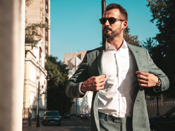 Portrait of handsome confident stylish hipster lambersexual model.Sexy modern man dressed in elegant suit. Fashion male posing in the street background in Europe city at sunset. In sunglasses - Zdjęcie, obraz