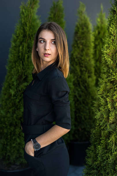 attractive young woman posing in black dress at nature, white cedar as background - Photo, image