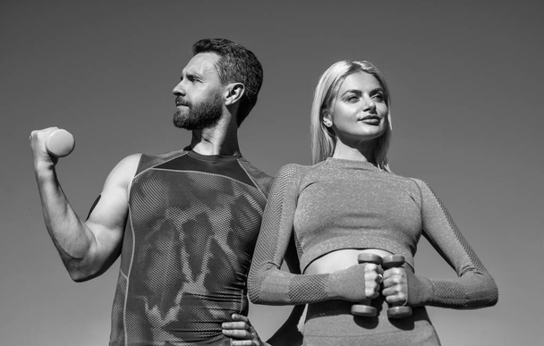 sport man and woman in sportswear training with dumbbells on sky background, fitness - Foto, Bild
