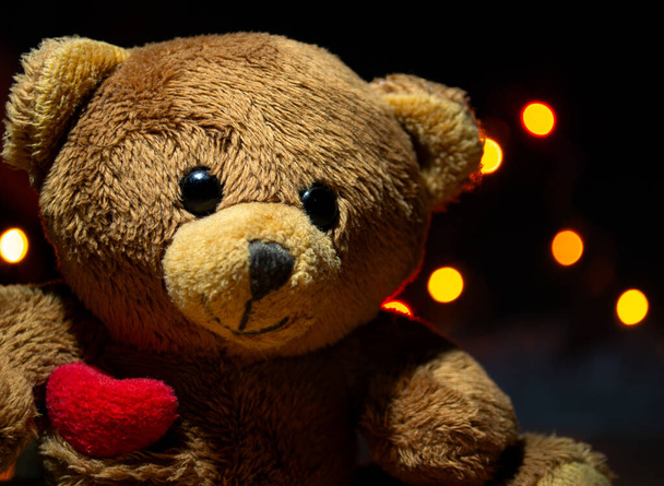 Brown teddy bear close up on the background of garland lights in bokeh - Fotografie, Obrázek