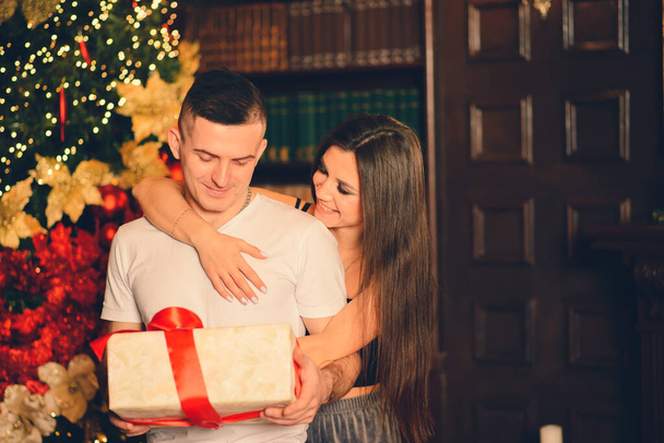 Хлопець дивиться на різдвяний подарунок, а його дівчина дарує йому поцілунок
 - Фото, зображення