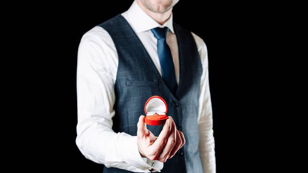 Heiraten Sie mich. Junger glücklicher Mann mit roter Geschenkbox mit diamantenem Verlobungsring, rotem Rosenstrauß. Verlobungsring - Foto, Bild