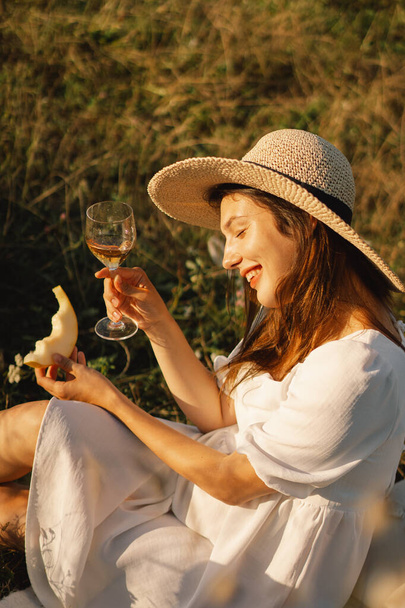 Mladá krásná dívka v bílých šatech s piknik se sklenkou šampaňského nebo bílého vína - Fotografie, Obrázek