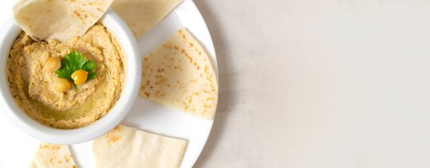 Hummus w ceramicznej białej misce z kawałkami pity na białej płytce na jasnym tle. Sztandar. Tradycyjne danie Bliskiego Wschodu. Orientacja pozioma. Koncepcja zdrowego żywienia. - Zdjęcie, obraz