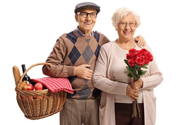 Elderly couple with a picnic basket and a bunch of red roses isolated on white background - Фото, зображення