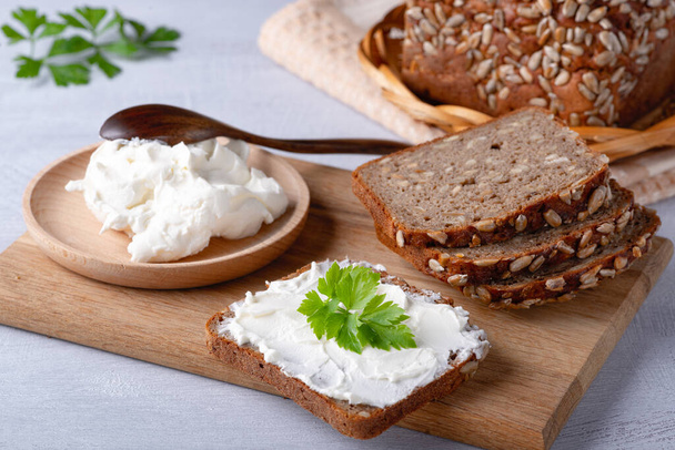 Çavdar ekmeği ahşap bir kesim tahtasının üzerinde peynir, ricotta ve otlarla.. - Fotoğraf, Görsel