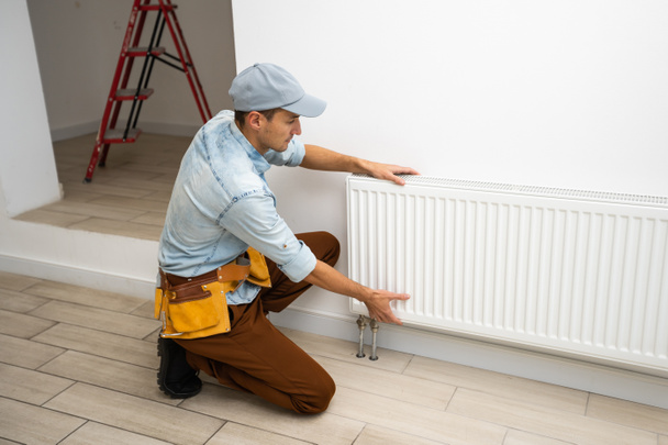 Un uomo cambia il riscaldamento in casa, radiatori. Il concetto di riscaldamento moderno, sostituzione del vecchio con uno nuovo. Calore in casa - Foto, immagini