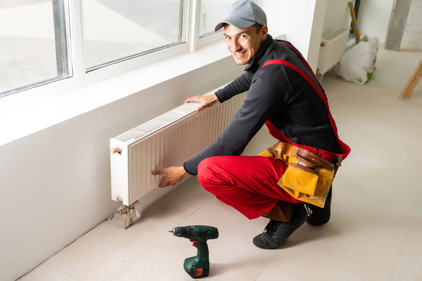 Workman montage radiateur de chauffage de l'eau près de la fenêtre dans le salon rénové blanc, Image avec espace de copie - Photo, image