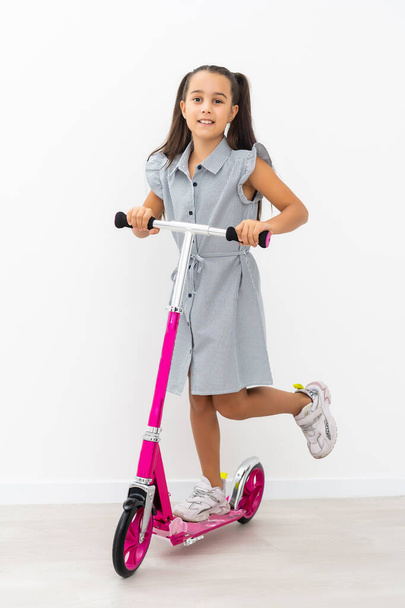 Happy little girl riding her scooter isolated on white. - Фото, зображення