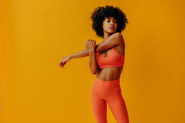 attractive young fit woman in sportswear stretching isolated on orange background - Photo, Image