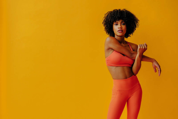 attractive young fit woman in sportswear stretching isolated on orange background  - Fotó, kép