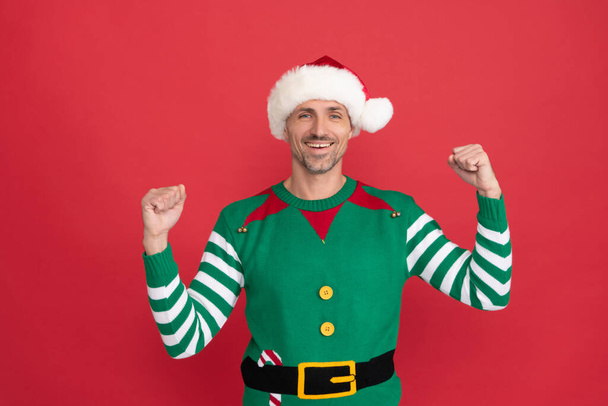 šťastný úspěšný muž v elfím kostýmu. xmas chlap v Santa Claus klobouk na červeném pozadí. - Fotografie, Obrázek