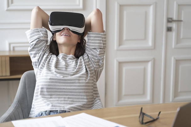 Młoda szczęśliwa pracownica w okularach VR w miejscu pracy ogląda filmy - Zdjęcie, obraz
