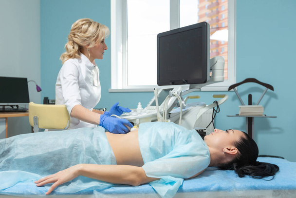 Doktor randevusu sırasında hamile kadının karnına ultrason sondası yerleştirirken çekilmiş fotoğraf. - Fotoğraf, Görsel