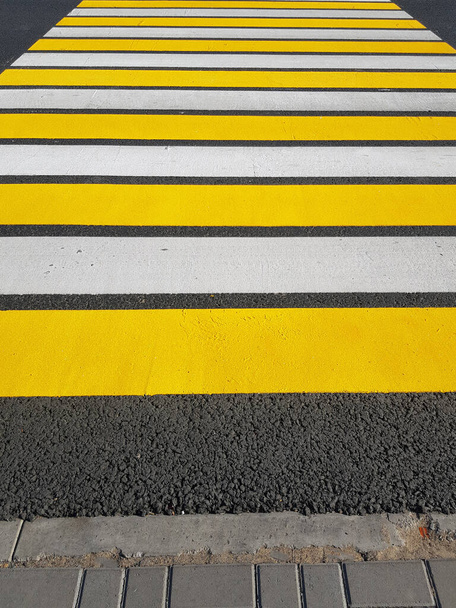 Vastamaalattu jalankulkijoiden risteys, jossa keltainen ja valkoinen merkintä asfaltissa, pystysuora kuva, auringonvalo. - Valokuva, kuva