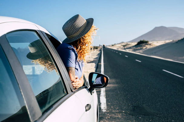 Kobieta przed oknem samochód zaparkowany na długiej asfaltowej stronie drogi podczas podróży. Letnia koncepcja podróży z kobieta podróżnik patrząc pustyni i gór z jej samochodu - Zdjęcie, obraz