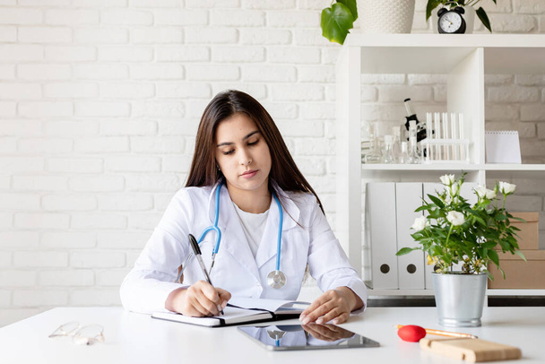 young female doctor write in journal filling medical history or anamnesis, woman nurse or GP make notes in notebook, finalize patient form or paperwork, healthcare, insurance concept - Photo, Image