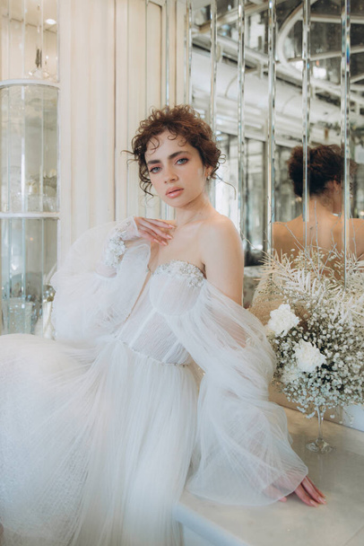 結婚式の装飾が施されたレストランで豪華なウェディングドレスを着た美しい巻き毛の花嫁 - 写真・画像