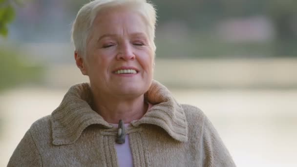 Boldog középkorú, ősz hajú nő, aki a szabadban álló kamerát nézi. Kellemes pozitív egyedülálló érett idős nyugdíjas hölgy széles fogú mosoly fejlövés portré, természetes régi szépség - Felvétel, videó