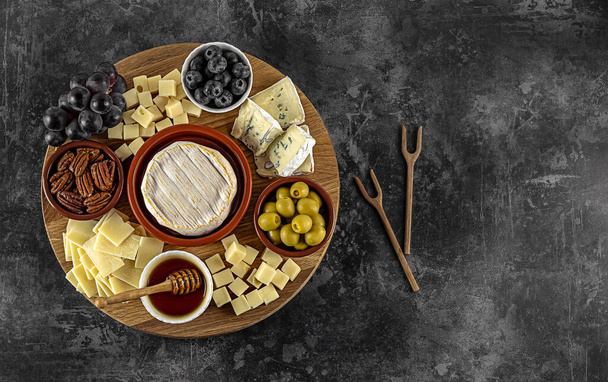Tasty cheese board with berries, honey, nuts, olives, and cheese varieties - Foto, Imagem