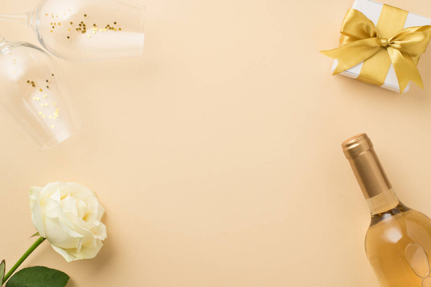 Top view photo of white rose two wineglasses with golden sequins bottle of white wine and white gift box with golden ribbon bow on isolated beige background with empty space in the middle - Fotó, kép