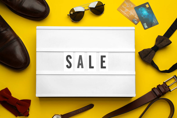 Light box with word Sale, men's accessories and credit cards on yellow background, flat lay - Фото, изображение
