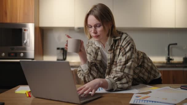Une jeune femme d'affaires magnifique travaille de la maison avec une tasse de café et regarde dans un écran d'ordinateur portable debout à la table. Voir le courrier et boire du café. Travail à distance depuis la maison - Séquence, vidéo