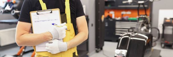 Auto mechanic in workshop holds clipboard for taking orders closeup - 写真・画像