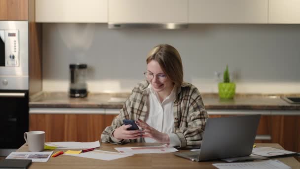 Een vrouw thuis met een mobiele telefoon en laptop kijkt en glimlacht - Video