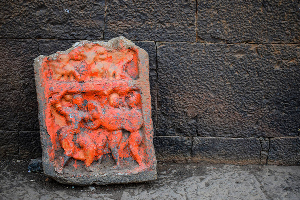 Hindistan, Mahrashtra 'da Kolhapur' da duvarın yanında tutulan safran rengine boyanmış savaşçıların oyulmuş granit taşını gösteren Antik harabe arkeolojik heykelin stok fotoğrafı. seçici odak . - Fotoğraf, Görsel