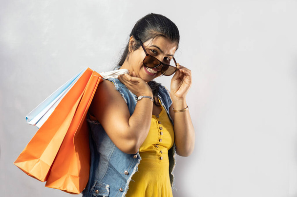 A beautiful Indian woman in yellow dress with shopping bags and big smile on white background - Valokuva, kuva
