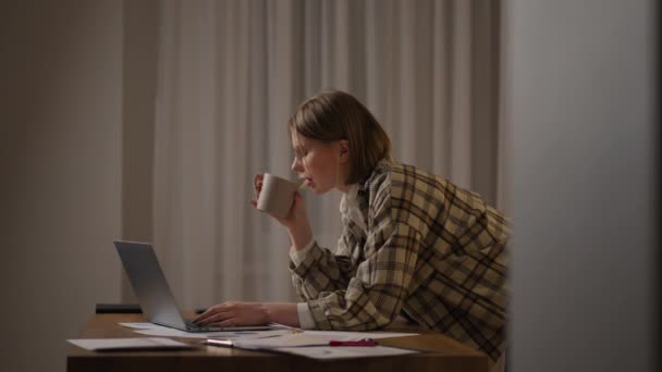 A girl works from home or a student is studying from home or a freelancer. She uses a laptop and a phone. girl sit at desk in living room study on laptop making notes, concentrated young woman work - Filmati, video
