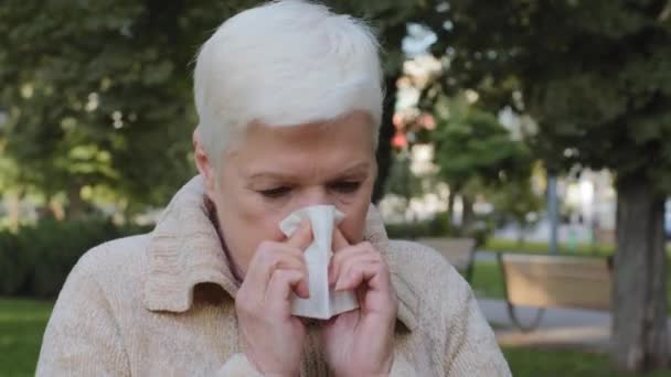 Allergic middle-aged lady feels unwell having flu symptom, ill old mature woman hold tissue sneezing got fever caught cold blowing running nose in handkerchief, sick. Allergy concept, closeup view - Footage, Video