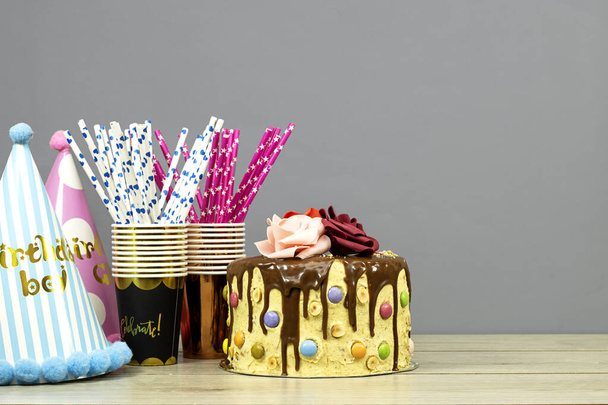 Gâteau d'anniversaire décoré de morceaux de chocolat et de texte joyeux anniversaire, de fleurs de noisettes et de roses et de tasses et pailles jetables sur une table en bois - Photo, image