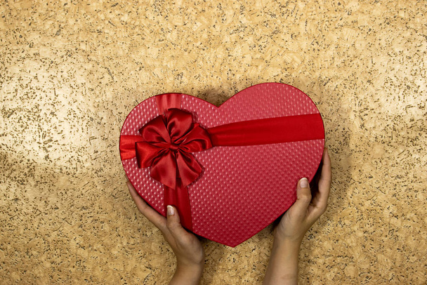 handen vrouw met rode hart vorm doos geïsoleerd op houten tafel, vakantie concept  - Foto, afbeelding