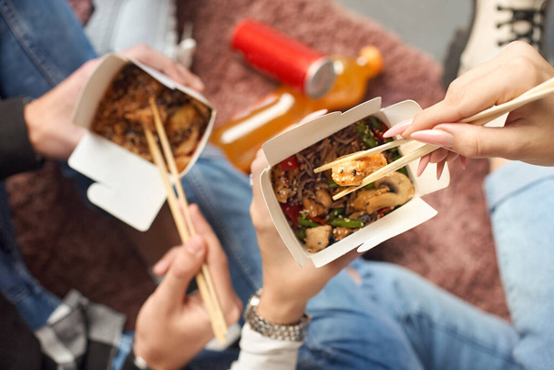 Closeup macro view of a delicious Wok Noodles with greenery in takeout paper box with chop sticks in the hands of friends - 写真・画像
